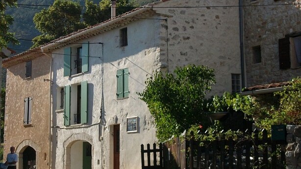 Un edificio rústico con fachada de piedra, contraventanas verdes y una pequeña entrada en arco.