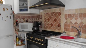 Una cocina con armarios blancos, una estufa negra, un microondas y una tabla de cortar roja sobre la encimera.