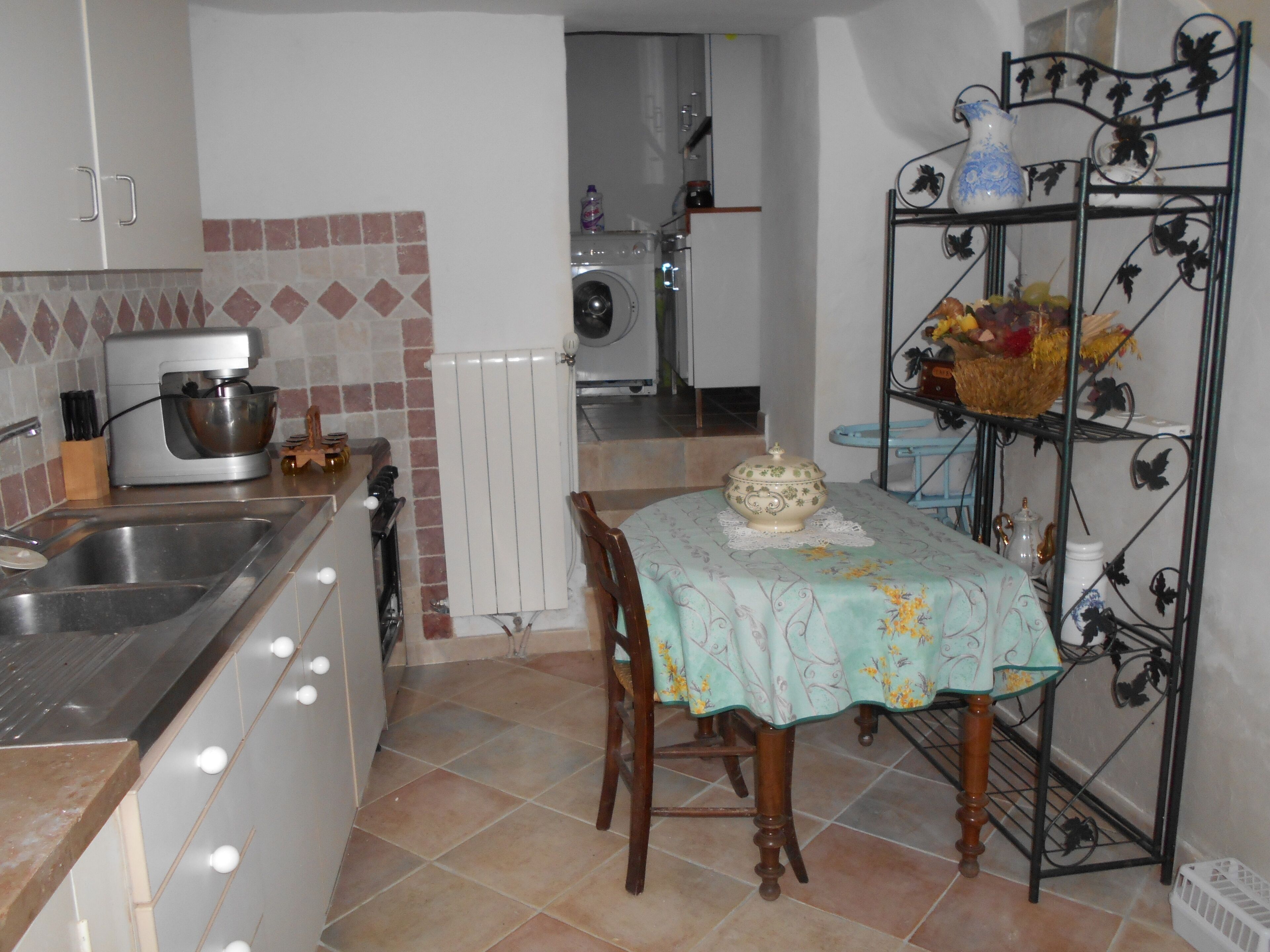 Une cuisine équipée d’un évier, d’un robot pâtissier, d’un radiateur et d’une table recouverte d’une nappe à motifs floraux.