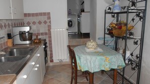 Una cocina con un lavamanos, un robot de cocina, un radiador y una mesa con mantel estampado.