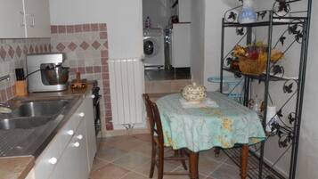 Une cuisine équipée d’un évier, d’un robot pâtissier, d’un radiateur et d’une table recouverte d’une nappe à motifs floraux.