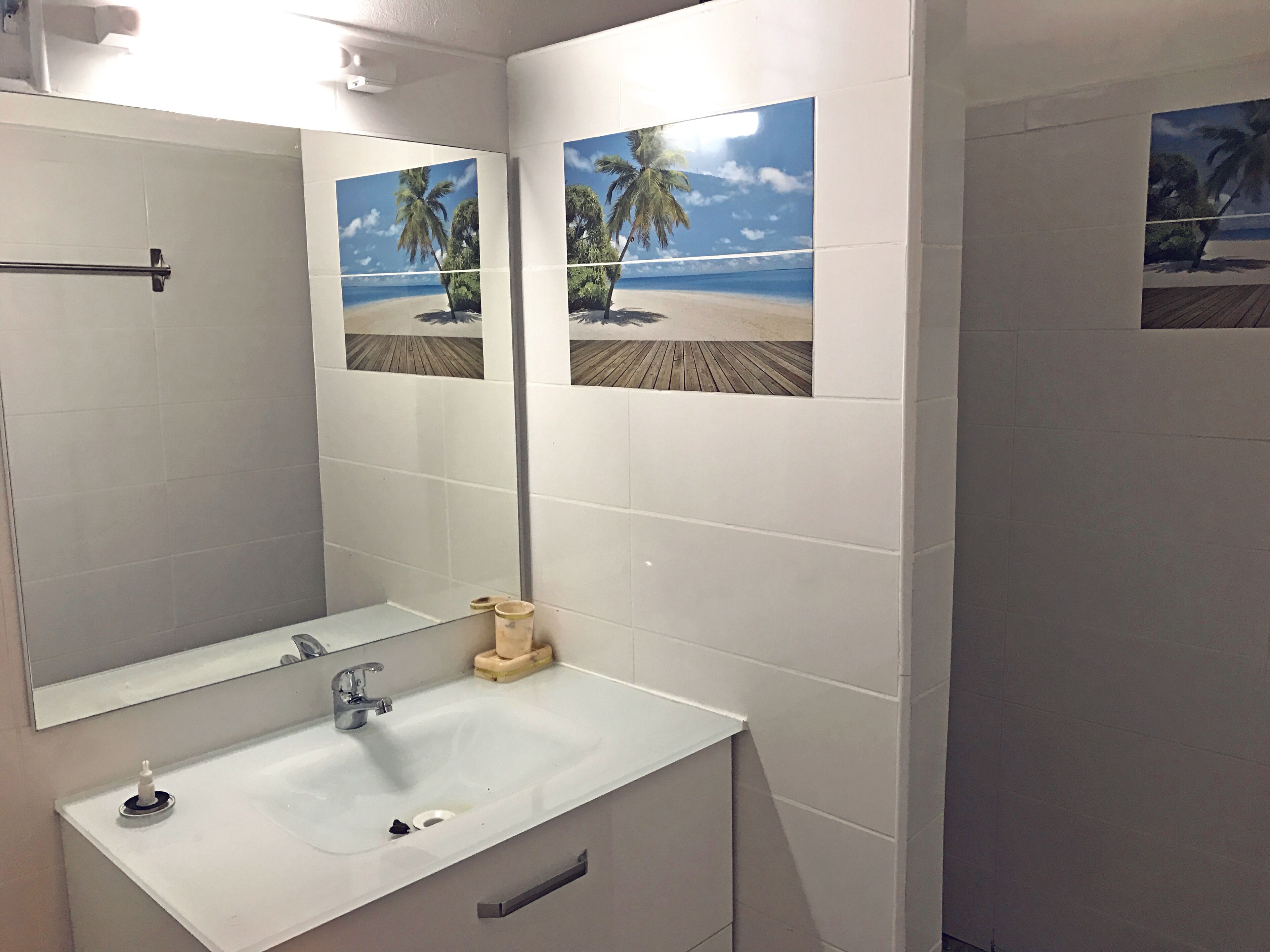 A bathroom with a white sink, mirror, and two framed pictures of a beach scene.