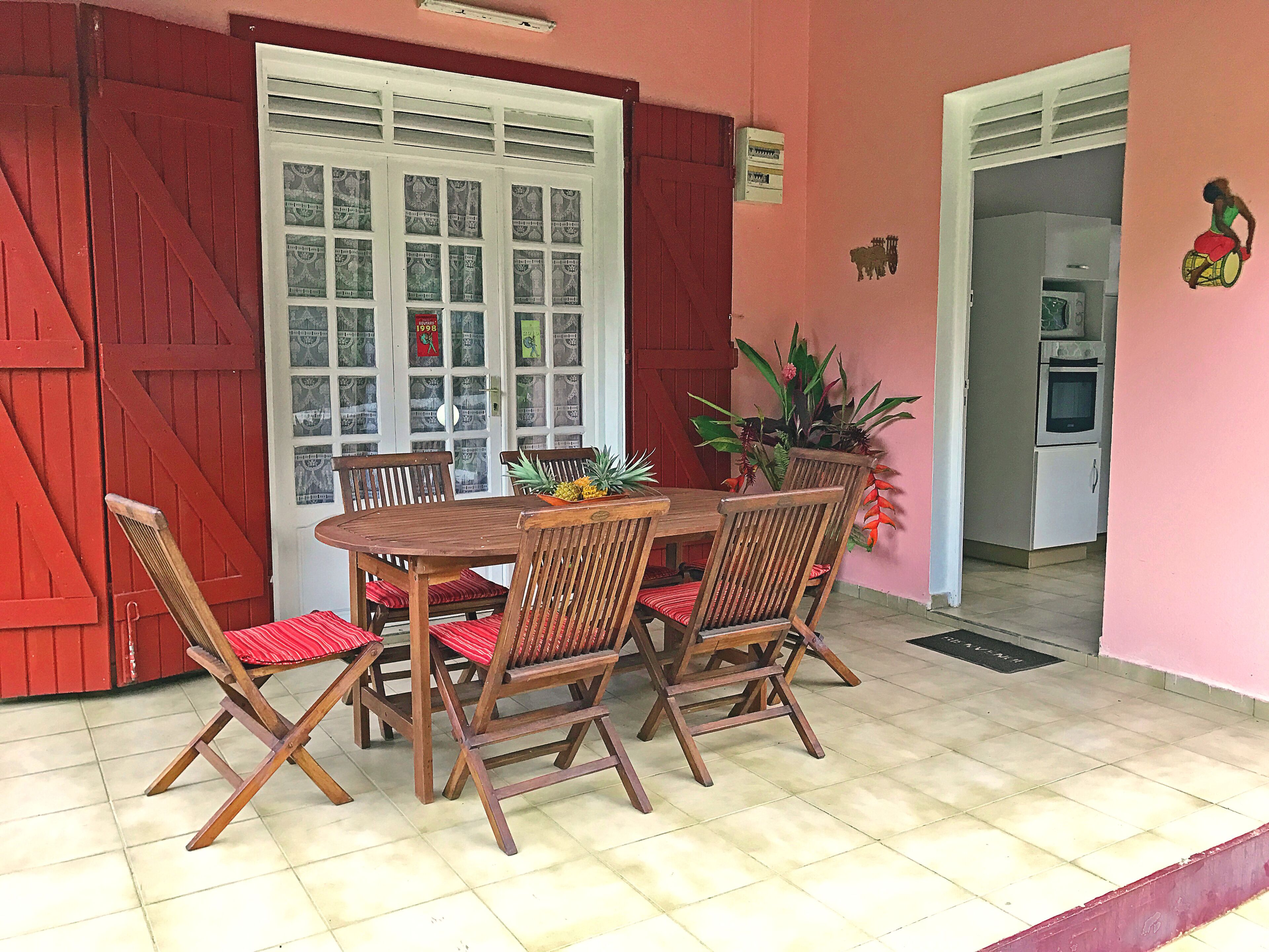 Un comedor con una mesa y sillas de madera, una planta en maceta y una puerta roja.