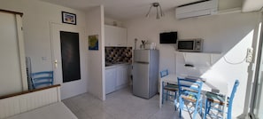 Une cuisine compacte avec des meubles blancs, un four à micro-ondes, un réfrigérateur et un coin repas avec des chaises bleues.