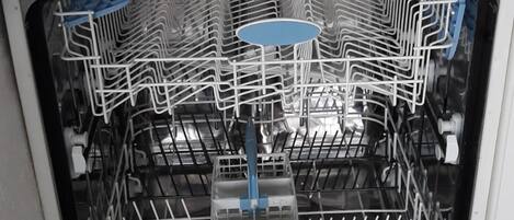 Un lave-vaisselle ouvert, avec ses étagères et ses ustensiles à l’intérieur, un évier de cuisine au-dessus, et un pare-éclaboussures carrelé.