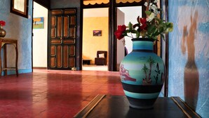 Un corridoio con pavimento piastrellato, una panca in legno, un vaso con fiori e una porta che conduce a un'altra stanza.