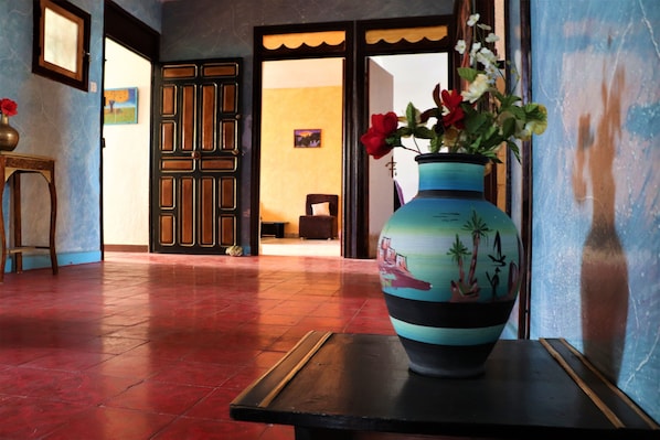 A hallway with a tiled floor, a wooden bench, a vase with flowers, and a door leading to another room.