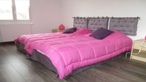 A bedroom with a large bed, a nightstand, a dresser, and a window with curtains.