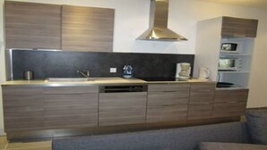 A modern kitchen with dark wood cabinets, a stainless steel range hood, and a built-in dishwasher.