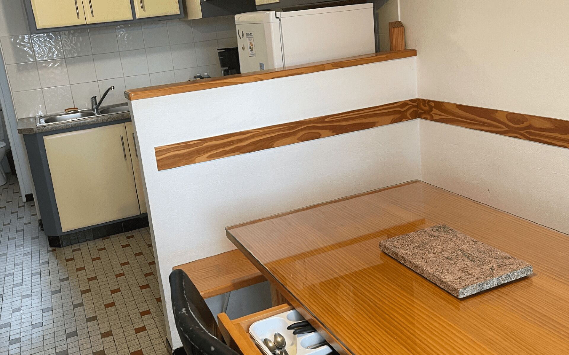 Una cocina compacta con una mesa de comedor de madera, un banco integrado y un refrigerador.