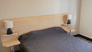 A bedroom with a wooden headboard, two bedside tables with lamps, and a grey bedspread. - Our gîtes are ideally located in Pontonx-sur-l'Adour (PONTONX-SUR-L'ADOUR)