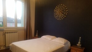 Une chambre à coucher comprenant un lit, une table de chevet, un élément de décoration murale, une fenêtre et un radiateur.