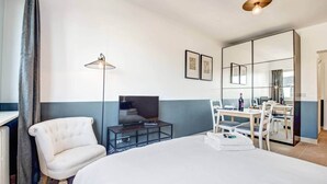 A hotel room with a large bed, a TV on a stand, a desk with a chair, and a dining area with a table and chairs. - Studio Chic super central near cathedral (Luxembourg)