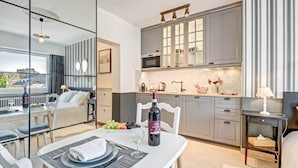 Une cuisine moderne avec un coin repas, comprenant une table dressée pour deux personnes avec des assiettes, une bouteille de vin et un saladier de fruits.