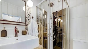 Une salle de bain moderne avec un grand lavabo blanc, une douche en verre et un miroir agrémenté d’un pare-splash décoratif en carreaux.