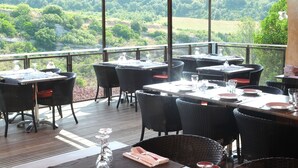 An outdoor dining area with tables and chairs, a view of a green landscape, and a red canopy.