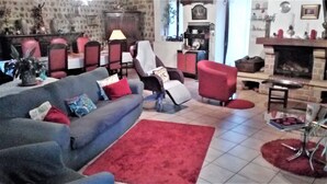 A living room with a blue sofa, red armchair, and a red rug. There is a fireplace and a dining area with a table and chairs. - GRANGE-GITE by ROCHEBARON (bas en basset)