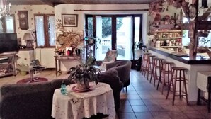 A cozy living room with a dining area, featuring a table with a floral tablecloth, a sofa, and a bar area with stools. - GRANGE-GITE by ROCHEBARON (bas en basset)