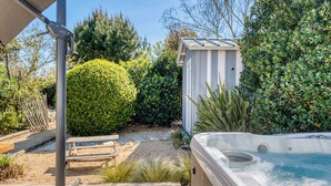 A hot tub, wooden deck, and a shed in a garden setting.