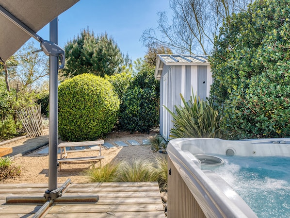 A hot tub, wooden deck, and a shed in a garden setting.