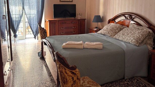 Un dormitorio con cama, televisor, candelabro, una silla y un cuadro en la pared.