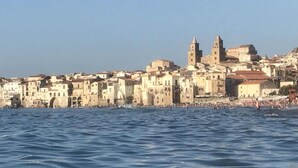 Un pueblo costero con edificios históricos, una iglesia destacada con dos torres y una playa con gente.
