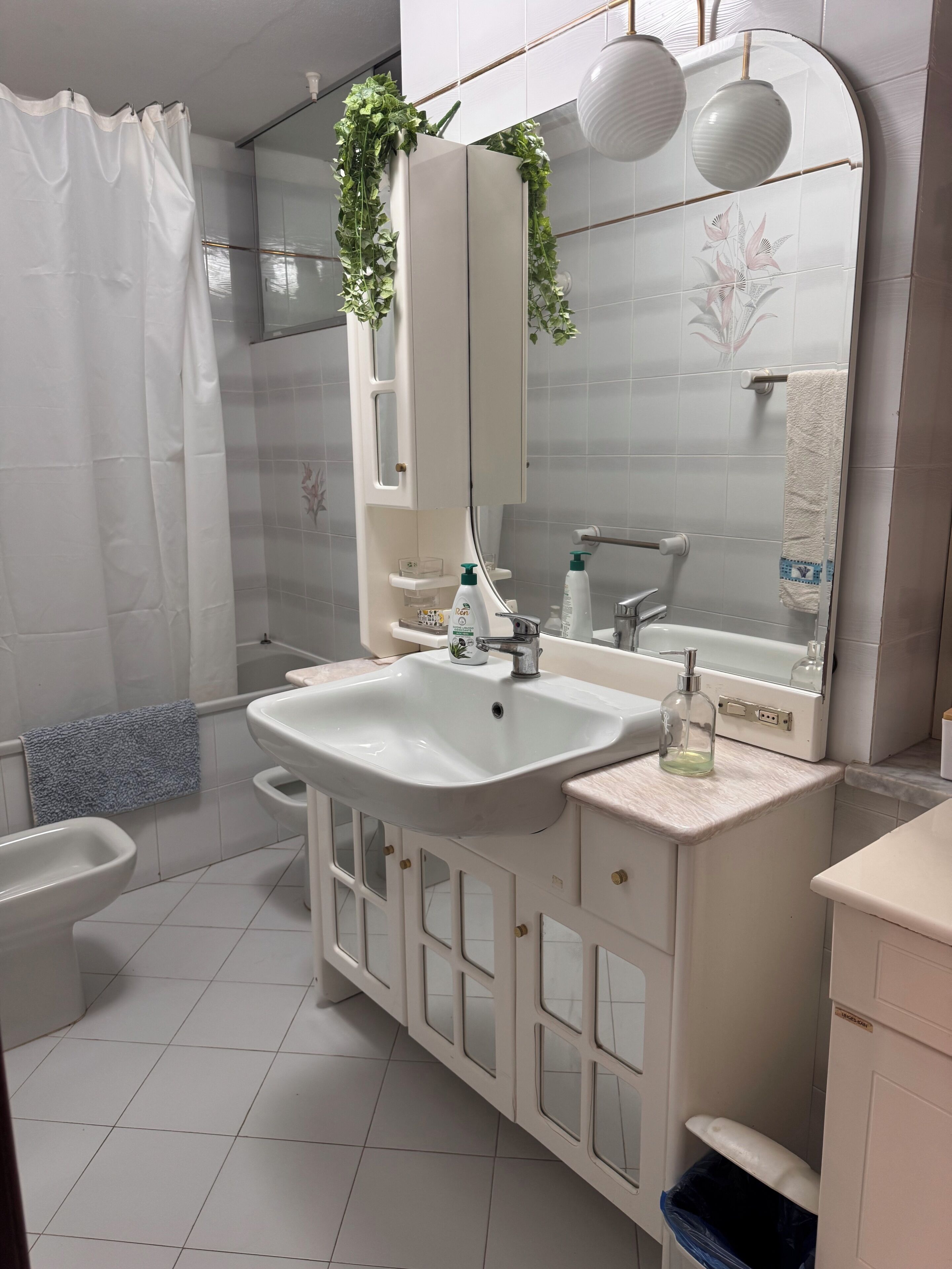 A modern bathroom with a white sink, mirror, and cabinet, a toilet, and a shower area.