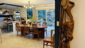 A dining area with a wooden table and chairs, a chandelier, and a view of the outdoors through large windows. - Beautiful 5* villa with exceptional sea view and secure swimming pool (Porto-vecchio)