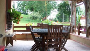 A covered patio with a wooden table and chairs, a hanging plant, and a view of a garden. - Pool, family rooms, breakfast (Seysses-Savès)