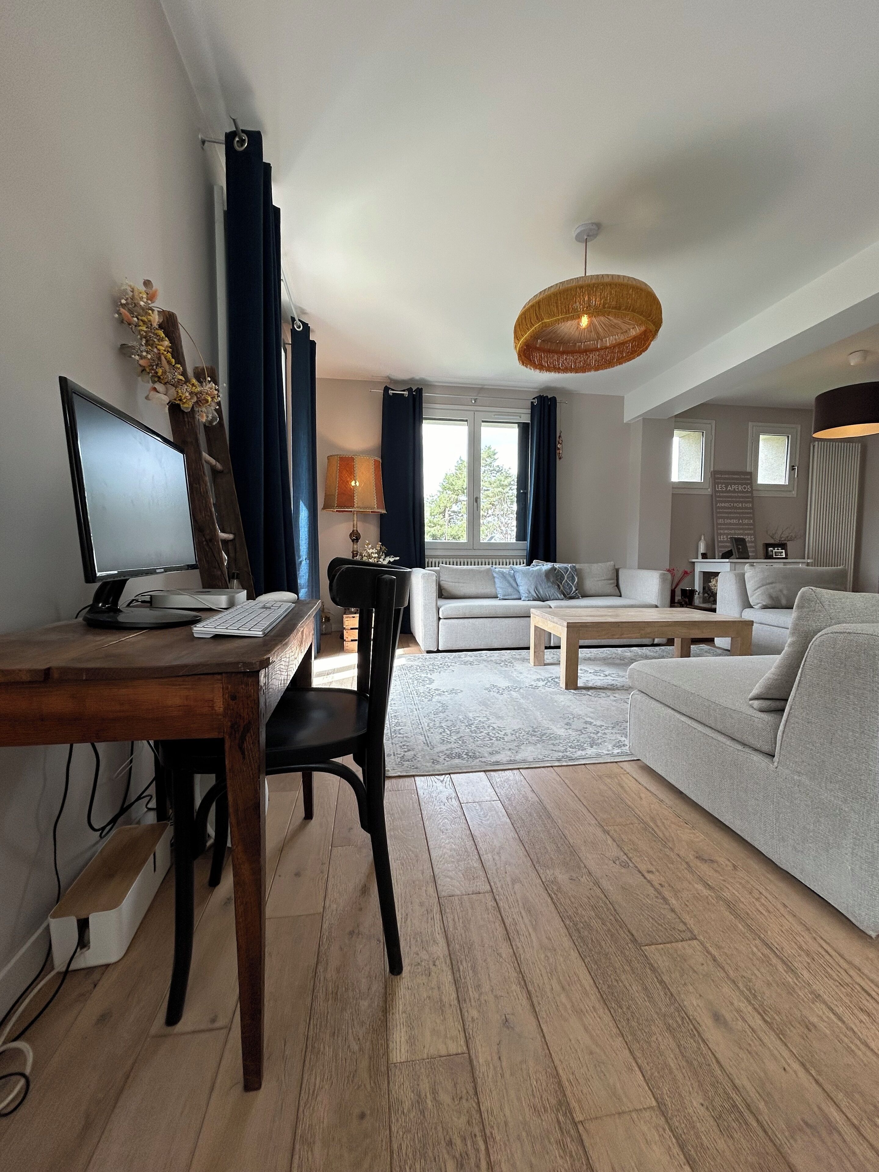 Un salon moderne avec un bureau en bois, un canapé gris et un coin repas.