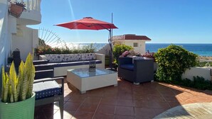 Un patio con mobiliario exterior, una sombrilla roja y vista al mar.