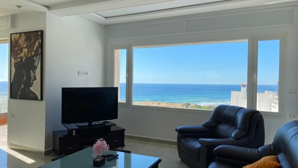 Una sala de estar moderna con un televisor grande, asientos cómodos y vista al océano.