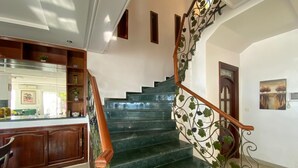 Una escalera con barandilla de madera y adornos metálicos, que lleva a un rellano con una puerta y un cuadro.