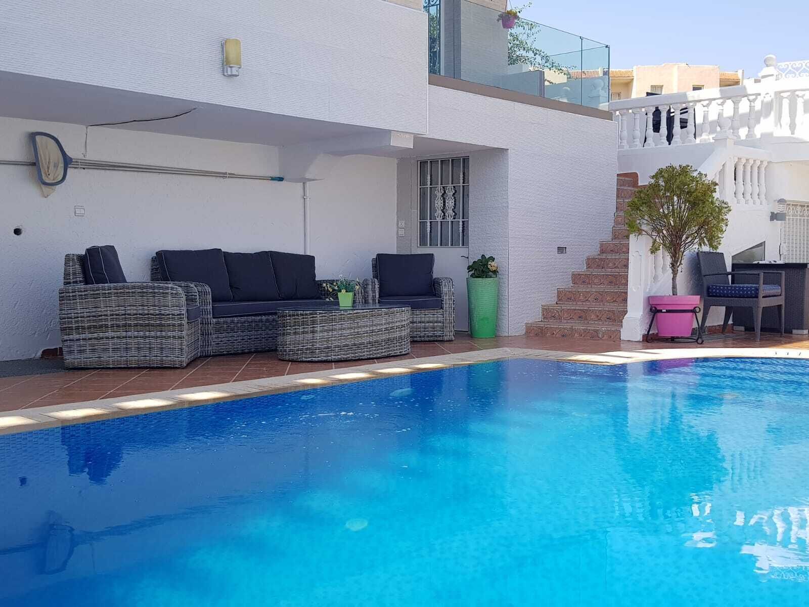 Un espace piscine extérieur moderne, doté d’un coin salon intégré et d’un escalier menant à un niveau supérieur.