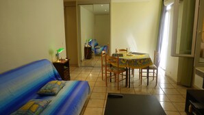 A living room with a sofa, a table with chairs, a TV, and a sliding door leading to another room. - Old Nice 41 m2 100 meters sea promenade / Saleya (Nice)