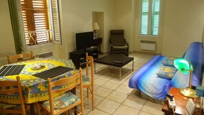 A room with a dining table, chairs, a sofa, a TV, and a lamp. - Old Nice 41 m2 100 meters sea promenade / Saleya (Nice)