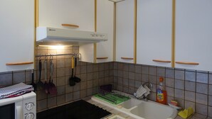 A kitchen with white cabinets, a stove, a sink, and various utensils hanging on the wall. - Old Nice 41 m2 100 meters sea promenade / Saleya (Nice)