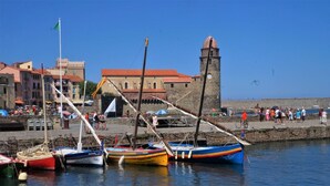 A harbor with boats docked, a stone tower, and a crowd of people on the promenade. - 110m2 of relaxation in the center, VISA, sun, sea and mountains (Perpignan)
