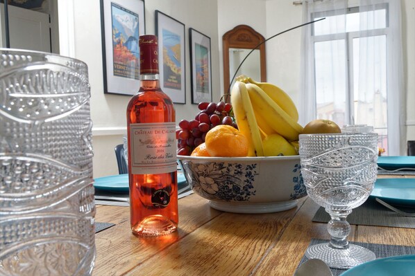 A dining table with a bottle of wine, a bowl of fruit, and crystal glasses.