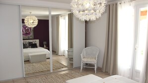 Ein Schlafzimmer mit einem großen Spiegel, einem weißen Bett, einem Sessel und einer Pendelleuchte.