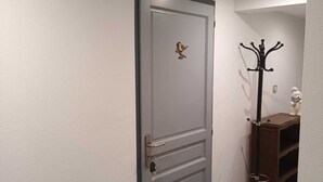 A hallway with a grey door featuring a bird decoration, a coat rack, and a small shelf with a teddy bear. -  in the village of Lapoutroie 10 km from Kaysersberg (Lapoutroie)