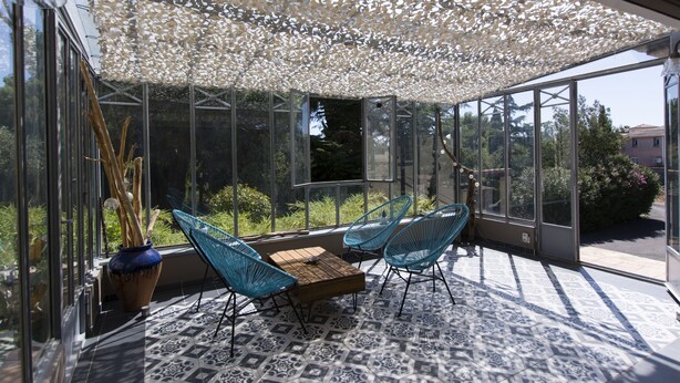 A sunlit patio with a patterned floor, a wooden table, and two blue chairs. - VILLA WITH COVERED SWIMMING POOL HEATED TO 28°, FULLY AIR CONDITIONED IN SERIGNAN (Sérignan)