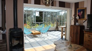 A room with a wood-burning stove, a glass door leading to an outdoor area with chairs and a table, and a television on a wooden cabinet. - VILLA WITH COVERED SWIMMING POOL HEATED TO 28°, FULLY AIR CONDITIONED IN SERIGNAN (Sérignan)