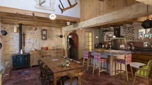 A rustic kitchen with a stone wall, wooden beams, and a large wooden table. - VILLA WITH COVERED SWIMMING POOL HEATED TO 28°, FULLY AIR CONDITIONED IN SERIGNAN (Sérignan)