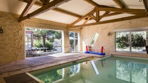 An indoor swimming pool with a clear view of the outside, wooden beams on the ceiling, and a tiled floor. - VILLA WITH COVERED SWIMMING POOL HEATED TO 28°, FULLY AIR CONDITIONED IN SERIGNAN (Sérignan)