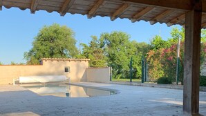 Un banc de fusta sota una zona coberta amb vista a una piscina i arbres.