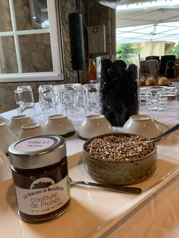 A table with various food items, including a jar labeled 'Les Vergers de Beaulieu confiture de Prunes', a bowl of prunes, and several glasses. - Gîte de groupe, 37 places, 13 rooms (La Romieu)