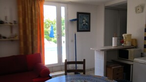 Een kamer met een rode bank, een eettafel met stoelen, een keukenhoek met een magnetron en een schilderij aan de muur.