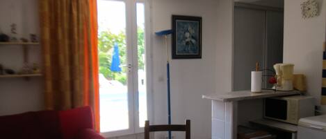 Una habitación con sofá rojo, una mesa de comedor con sillas, una zona de cocina con microondas y un cuadro en la pared.