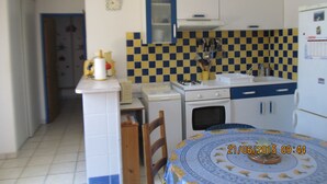 Een kleine keuken met een fornuis, spoelbak en een klein oven. Er staat een eettafel met een tafelkleed met patroon.